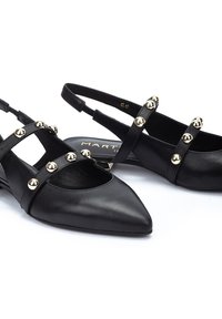 Zapatos slingback de cuero negro con puntas afiladas, adornados con tachuelas decorativas en tono dorado en las correas. Textura suave y diseño minimalista.