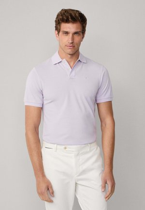 Helllila Poloshirt mit Kragen und kurzen Ärmeln, aus einem glatten Stoff gefertigt. Kombiniert mit weißen Hosen, die über ein dezentes Taillenbündchen verfügen.