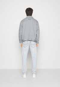 Randig denimjacka i grått och vitt, med avslappnad passform och klassisk krage, tillsammans med ljusblå jeans och vita sneakers.