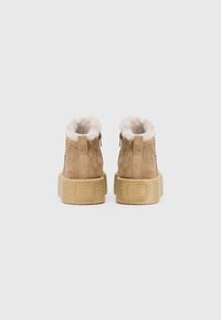 Stivaletti alla caviglia in suede beige con suola testurizzata, fodera in pelliccia sintetica e zip posteriore. I dettagli cuciti sui lati aggiungono interesse al design.