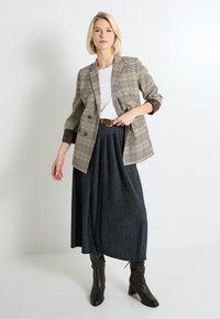 Blazer a rayas de doble botonadura en marrón y crema, combinado con una camiseta blanca y una falda negra con pliegues. Botas de tacón marrones completan el look.