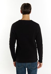 Tricou negru texturat cu un design ribat, mâneci lungi și decolteu rotund, asortat cu blugi din denim albastru. Detaliu vizibil de cusătură.