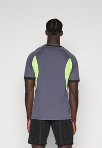 Grå atletisk t-skjorte med neongrønne aksenter og svart kant, med en figursydd design og teksturerte seksjoner på skuldrene.
