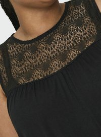 Juoda suknelė su permatomu nėrinių viršumi, papuoštu sudėtingais raštais, ir minkštu, tekstūriniu apatiniu skyriumi, sukurta su apvaliu iškirpimu.