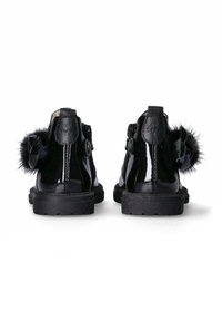 Stivali in vernice nera con suola testurizzata, dotati di un fiocco decorativo nero e un accento di pelliccia artificiale sul retro.