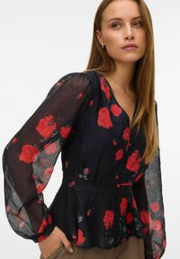 Musta kukallinen paita, jossa on punaisia ruusuja, läpinäkyvät pitkät hihat, V-mallinen kaula-aukko, nappituki, peplum-vyötärö, kevyt kangas, virtaava rakenne.