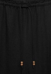 Black drawstring pants made of fabric with a smooth texture. Features a gathered waistband and wooden bead accents on the drawstring.