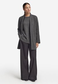 Grå stickad tröja lager på lager under en lång grå kofta, kombinerad med vida grå byxor och svarta, texturerade skor. Enkelt, elegant design.