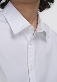 Witte overhemdo met een spread collar, voorzien van een gladde katoenen textuur en zichtbare stiksels langs de kraag en knopenrij.
