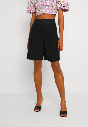 Black knee-length shorts, featuring a relaxed fit, elastic waistband, and smooth fabric texture. Worn with a floral cropped top and black sandals.