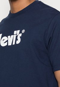 Mörkblå bomullströja med korta ärmar och rund halsringning, med en stor vit "Levi's"-logotyp över bröstet.