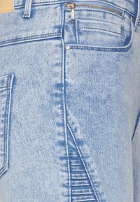 Jeans de denim azul claro com um design elegante, textura subtil, um bolso com fecho e um detalhe de costura em camadas distintivo.