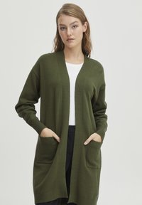 Cardigan vert olive en matériau doux, avec un col en V, des manches longues, des poches latérales et une coupe décontractée.