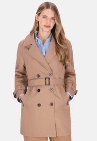 Palton bej cu design cu două rânduri de nasturi, rever mare, curea în talie și manșete cu nasturi. Dispune de buzunare laterale.