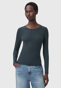 Maglietta a maniche lunghe di colore verde scuro a coste con scollo rotondo, silhouette aderente e texture morbida abbinata a jeans in denim azzurro chiaro a gamba larga.
