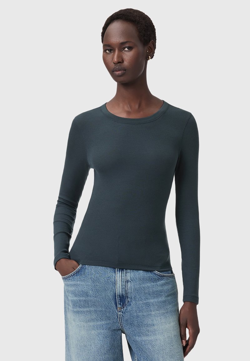 Maglietta a maniche lunghe di colore verde scuro a coste con scollo rotondo, silhouette aderente e texture morbida abbinata a jeans in denim azzurro chiaro a gamba larga.