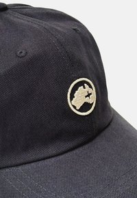 Gorra de béisbol azul marino con una textura de tela sólida, que presenta un parche bordado circular en beige que representa un contorno de mapa.