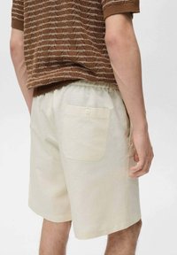 Beige shorts met een elastische tailleband en een enkele achterzak, gemaakt van een lichte stof. Heeft een gladde textuur en een comfortabele pasvorm.