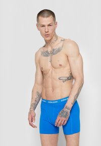 Kék férfi boxeralsó, testhezálló fazonban, fehér gumírozott derékkal, amelyen a "BJÖRN BORG" felirat szerepel. Sima anyag, letisztult dizájn, minta nélkül.
