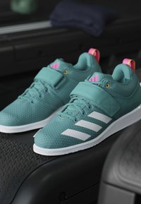 Jasné perforované športové topánky v odtieni teal s bielou podrážkou, tromi bielymi pruhmi, suchým zipsom a ružovými akcentmi na päte. Odolný materiál a textúrový povrch.
