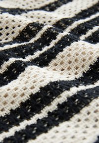 Tissu en crochet noir et blanc avec des rayures texturées alternées et des motifs à tissage ouvert, présenté en doux plis.