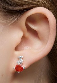 Orecchini in argento con una pietra ovale rossa e due piccoli dettagli in argento, incastonati contro l'orecchio. Texture liscia e finitura lucida.