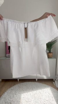 Top blanco de tirantes caídos con bordes de encaje, tejido ligero, escote elástico y ajuste holgado. Fluye suavemente hasta la mitad de la longitud.
