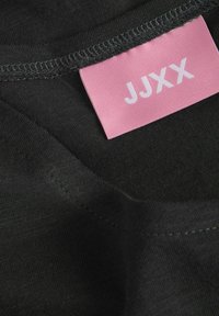 Tela de algodón negra con una textura suave, que presenta una etiqueta rosa con "JJXX" impresa en blanco. Cortada con un cuello redondo y costuras en contraste.