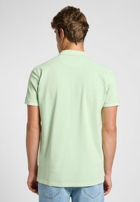 Minttuvihreä lyhythihainen polo-paita, jossa on ribbauskaulus, rento istuvuus ja sileä puuvillapinta. Takana on tukeva pinta ja hienovaraiset ompeluyksityiskohdat.