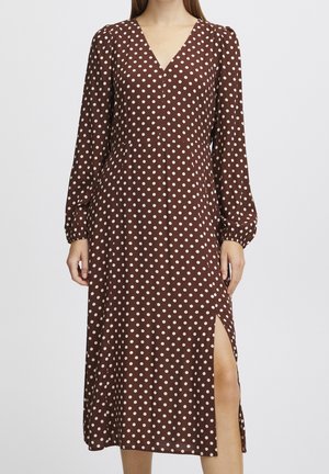 Brown midi dress with white polka dots, long puffed sleeves, V-neck, elastic cuffs, and a side slit revealing the leg.
