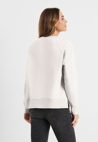 Lichtgrijze sweatshirt met ronde hals en lange mouwen, voorzien van ribbels aan de cuffs en zoom. gedragen met donkergrijze jeans met een gladde textuur.