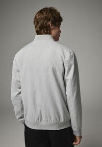 Jacheta bomber gri deschis, cu o textură netedă, manșete ribbate și un tiv elastic. Design simplu, fără modele sau embellishments vizibile.