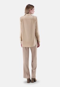 Camicia beige a maniche lunghe con colletto, texture liscia e polsini abbottonati, abbinata a pantaloni beige chiaro e calzature con tacco.