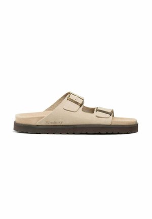 Beige suede sandals with two adjustable straps and metallic buckles. Low-profile, contoured sole in brown with textured tread for grip.