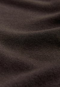 Közelkép puha, sötétbarna kötött anyagról, amely finom, egyenletes textúrát és finom hajtásokat mutat.