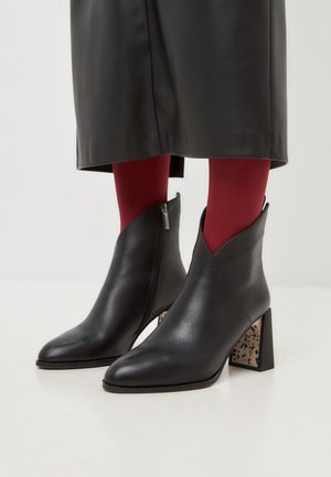 Schwarze Lederknöchelstiefel mit Blockabsätzen und gesprenkeltem Muster, getragen mit roten Strumpfhosen und einem schwarzen Lederrock.