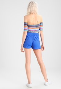 Colorful striped off-the-shoulder top with ribbed texture, paired with blue athletic shorts. Visible elastic waistband and white sneakers.