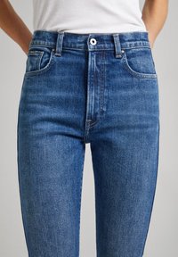 Högmidjade blå denimjeans med femfickdesign, lätt slitage och kopparstickningar. Slät struktur, smal passform.