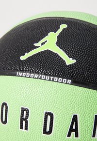Grøn og sort gummibasketbold med struktureret overflade, et fremtrædende Jumpman-logo og en "INDOOR/OUTDOOR"-mærkat på en sort kant.