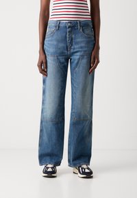 Wide-leg blue denim jeans featuring contrast stitching and two front pockets. Pairing with navy and cream sneakers for a casual look.