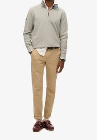 Felpa grigia con colletto a metà zip, chinos beige e scarpe marroni. Tra le caratteristiche salienti ci sono il colletto a contrasto e i risvolti dei pantaloni.