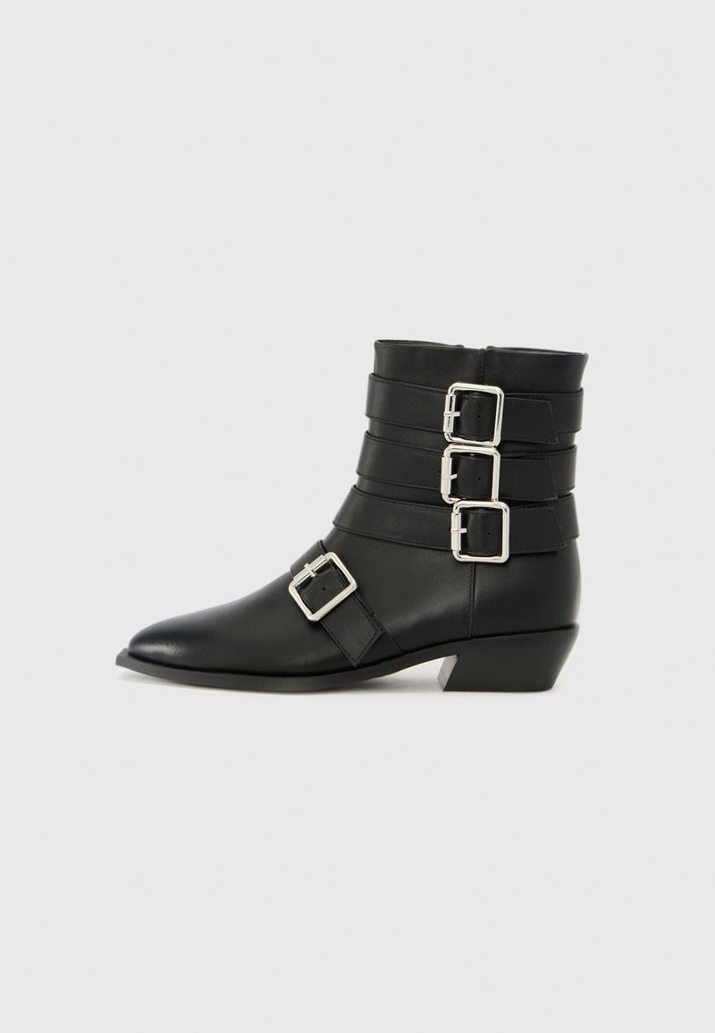 Bottine en cuir noir avec des brides empilées ornées de trois boucles argentées, bout pointu et petit talon carré. Texture lisse sur toute la surface.
