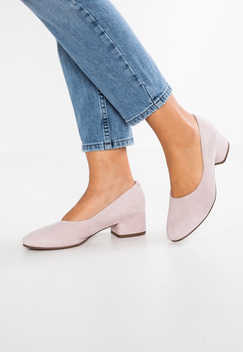 Chaussures à talons carrés en daim rose clair avec un bout arrondi et une texture lisse, associées à un jean en denim bleu retroussé.