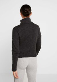 Černá zkrácená bunda s vysokým límcem, texturovanou tkaninou a dlouhými rukávy. Záda mají detail švu a bunda je na pasu přiléhavá.