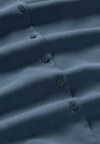 Tejido azul oscuro con una textura suave, que presenta múltiples cierres de botones en un color a juego y costuras verticales sutiles.