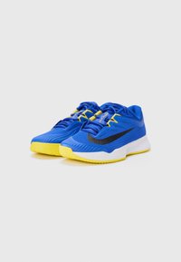 Blå idrettssko med gule detaljer, teksturert mesh-overdel, svart side-swoosh og hvit såle med et sikksakmønster.