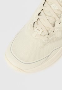 Αθλητικό παπούτσι σε ανοιχτό μπεζ χρώμα με υφασμένο πάνω μέρος από δίχτ�υ με υφή, ραφές σε αντίθεση, λεπτά κορδόνια και μαλακή σόλα με διακριτικά καμπυλωτό σχήμα.