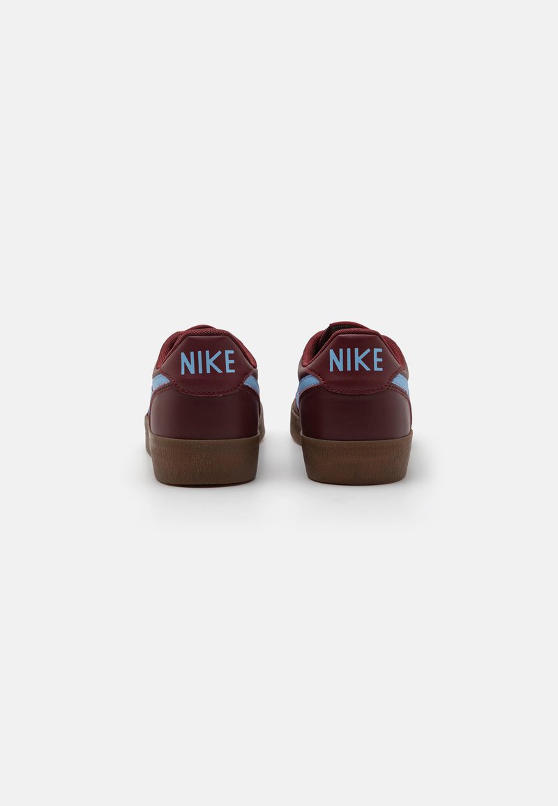 Zapatillas de cuero burdeos con detalles en azul claro, forma redondeada, cuello acolchado y suela de goma marrón. Presentan el logotipo "NIKE" en el talón.