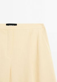 Jupe beige clair taille haute avec poches latérales, texture lisse et une étiquette de marque noire visible à l'intérieur de la ceinture.