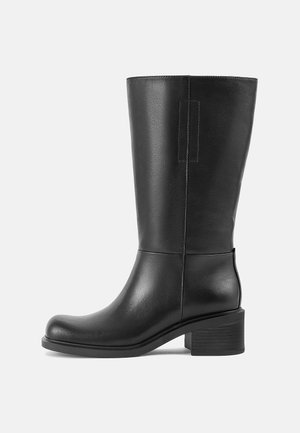 Botte noire en cuir mi-mollet avec talon bloc, bout arrondi et détail de languette de tirage, vue de côté gauche sur fond uni.